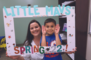 Priscila Tamplain and young boy holding a Little Mavs cutout picture frame smiling