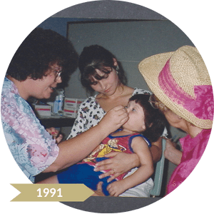 Three women gathered around a child giving it medicine